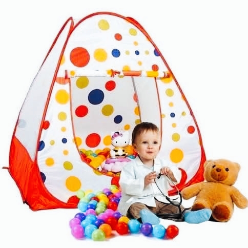 A realistic photo of a young child dressed as a doctor, holding a stethoscope while sitting in front of a colorful polka-dot play tent with a teddy bear and scattered toy balls. Little Doctor Playing with Colorful Tent and Teddy Bear